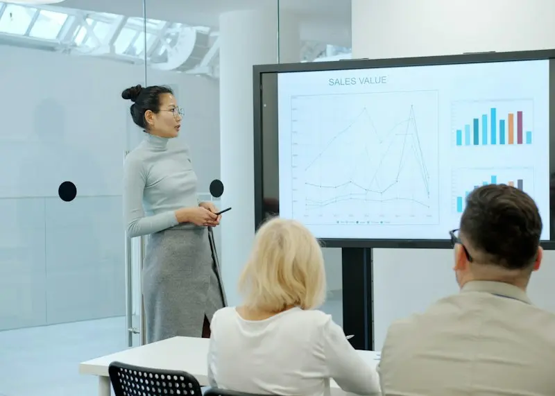 Woman presenting sales data on a screen to seated colleagues
